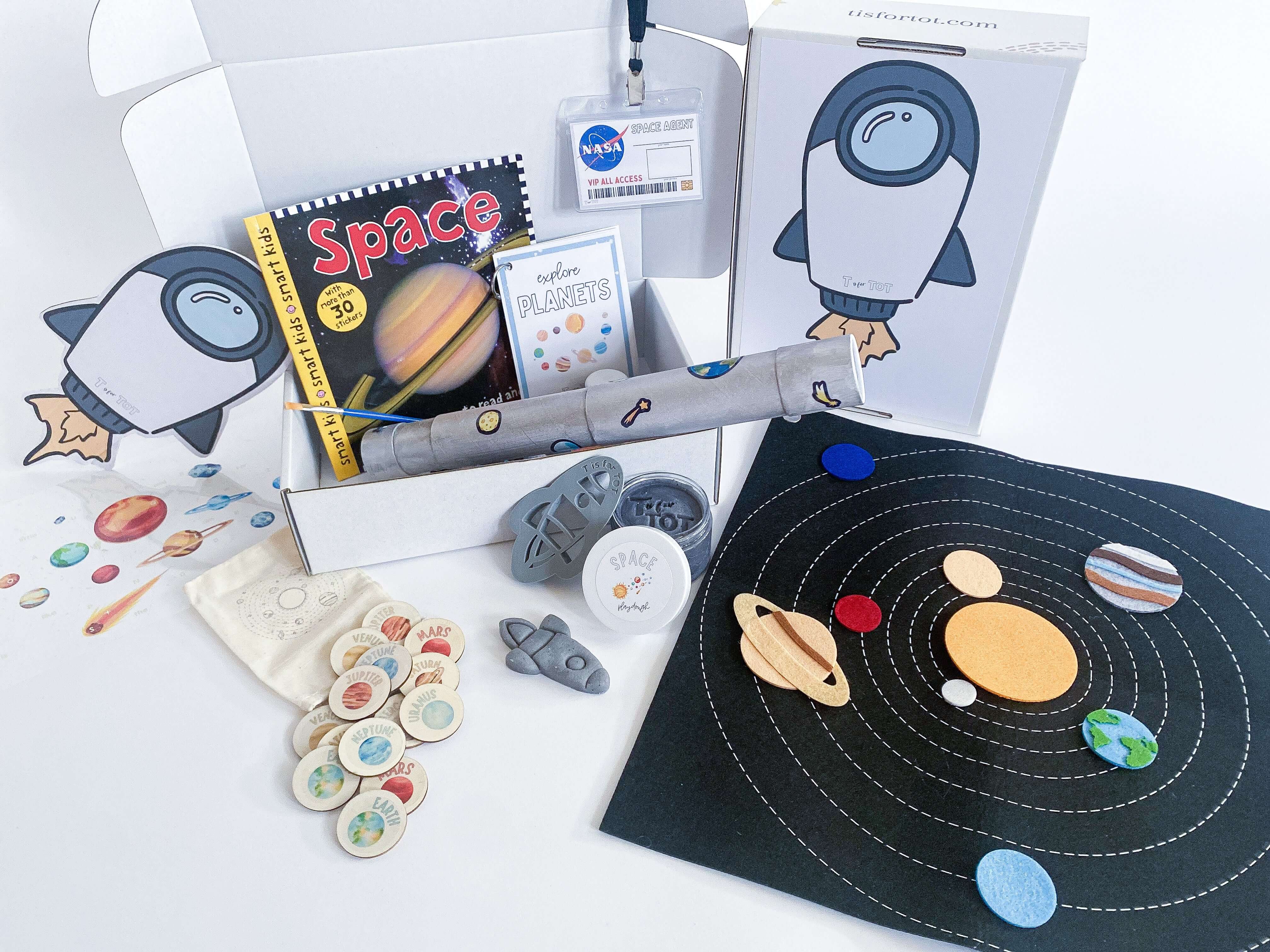Space-themed play kit for kids with homemade playdough, rocket playdough cutter, and custom-made felt space mat. Includes telescope activity, wooden planet memory game, NASA name badge, STEAM recipe card, and a box that turns into a rocket backpack. Perfect for creative play and learning.